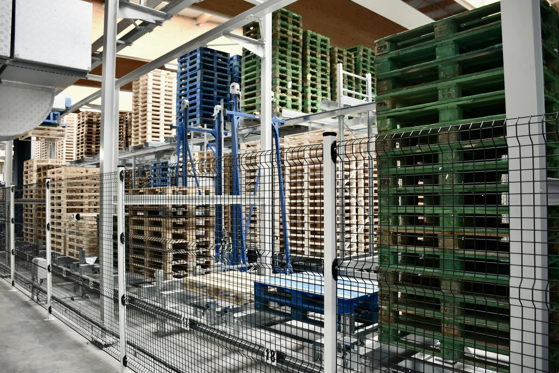 Opgelegde pallets in een magazijn, gescheiden door een metalen hekwerk voor veiligheid