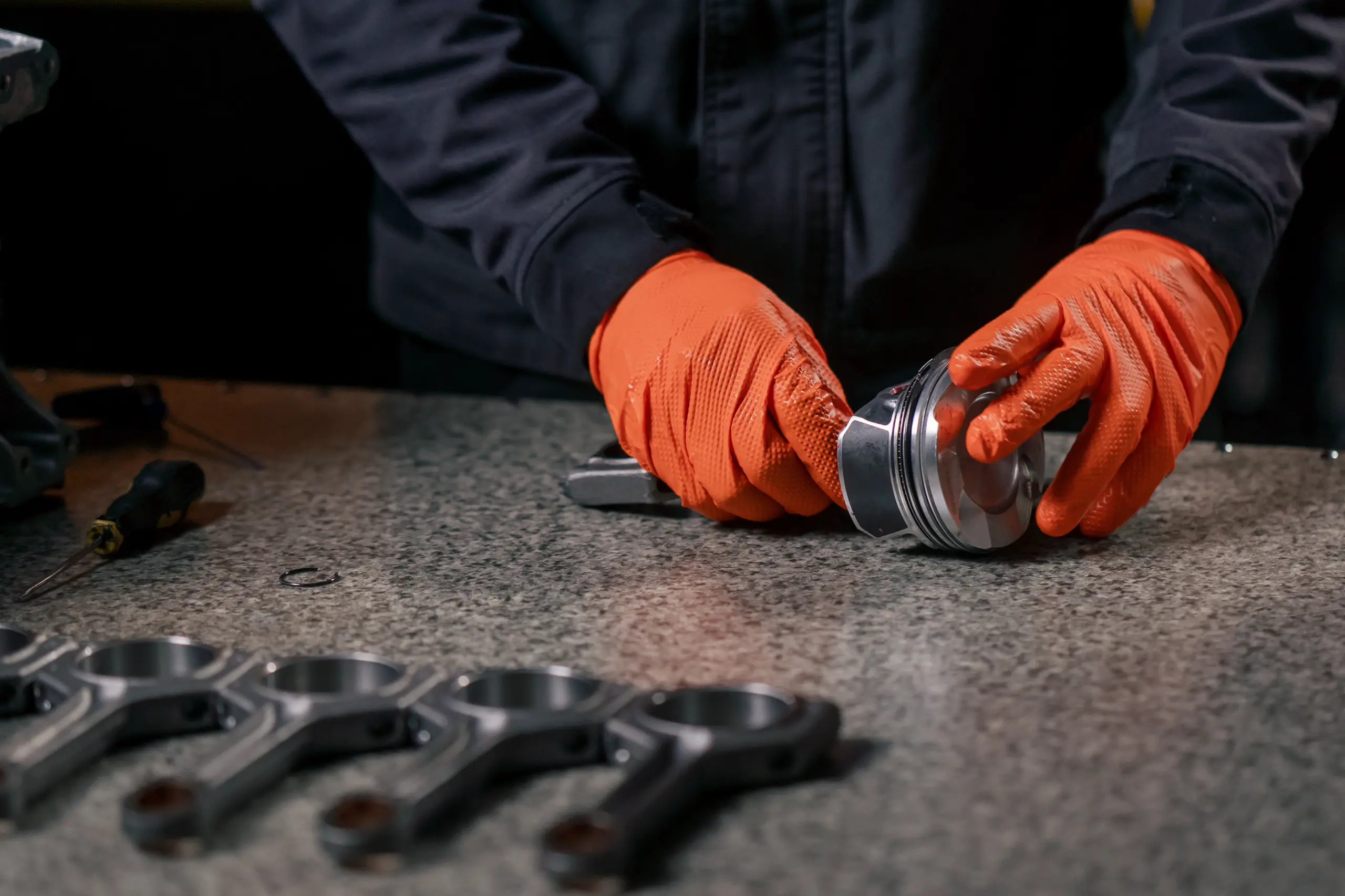 Een monteur met oranje handschoenen monteert een cilinderkop op een werktafel met gereedschap op de achtergrond