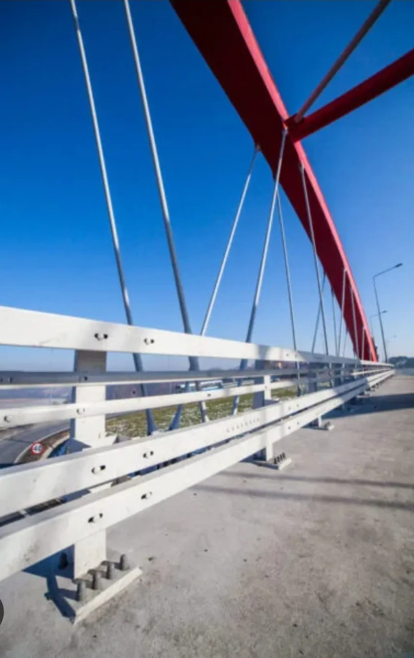 Een modern stalen brug met rode leuningen onder een blauwe lucht