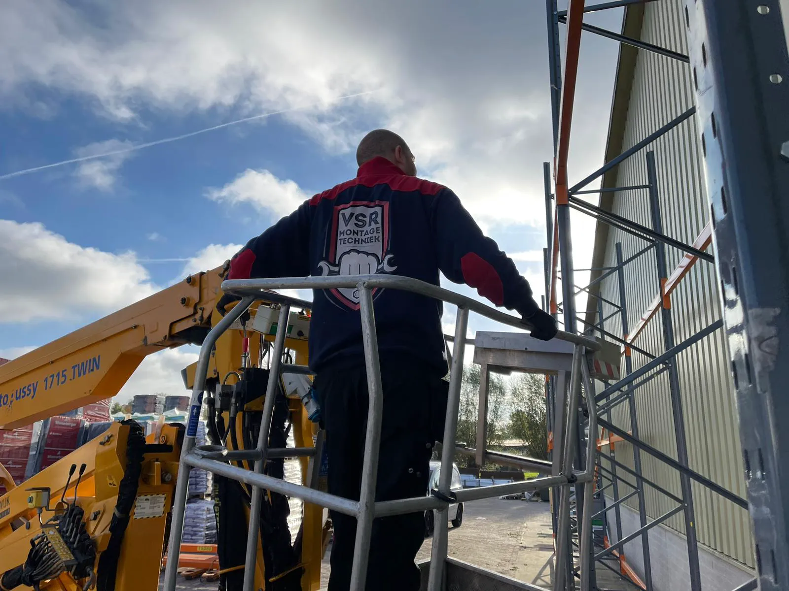 Een werknemer van VSR MONTAGE TECHNIEK werkt aan stellingbouw vanaf een hoogwerker