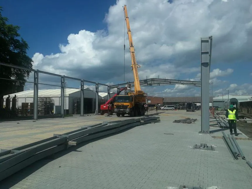 Kraan monteert stalen constructie op een bouwlocatie, met medewerkers in veiligheidskleding