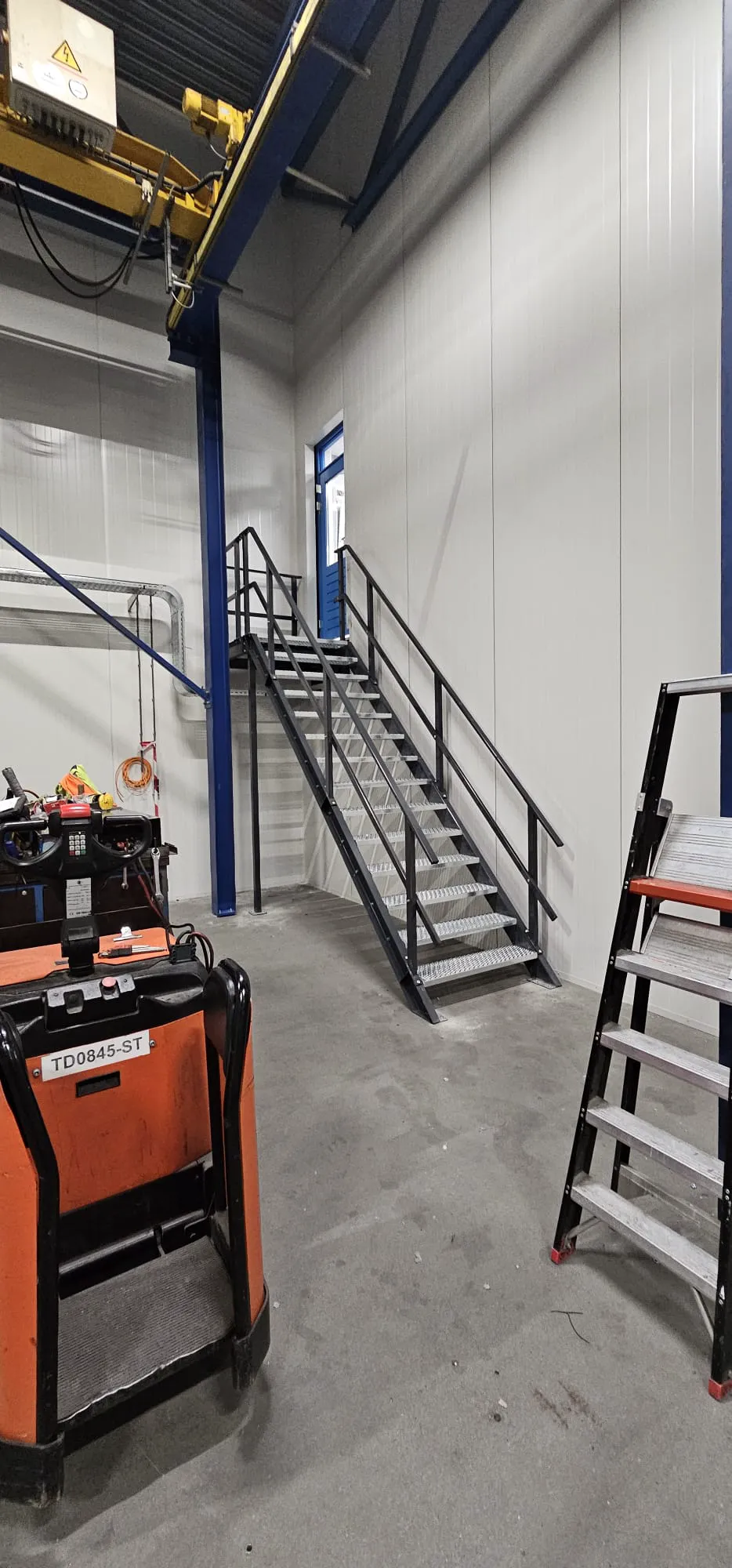 Stalen trap met leuningen in een magazijnruimte met gereedschap en ladder op de voorgrond