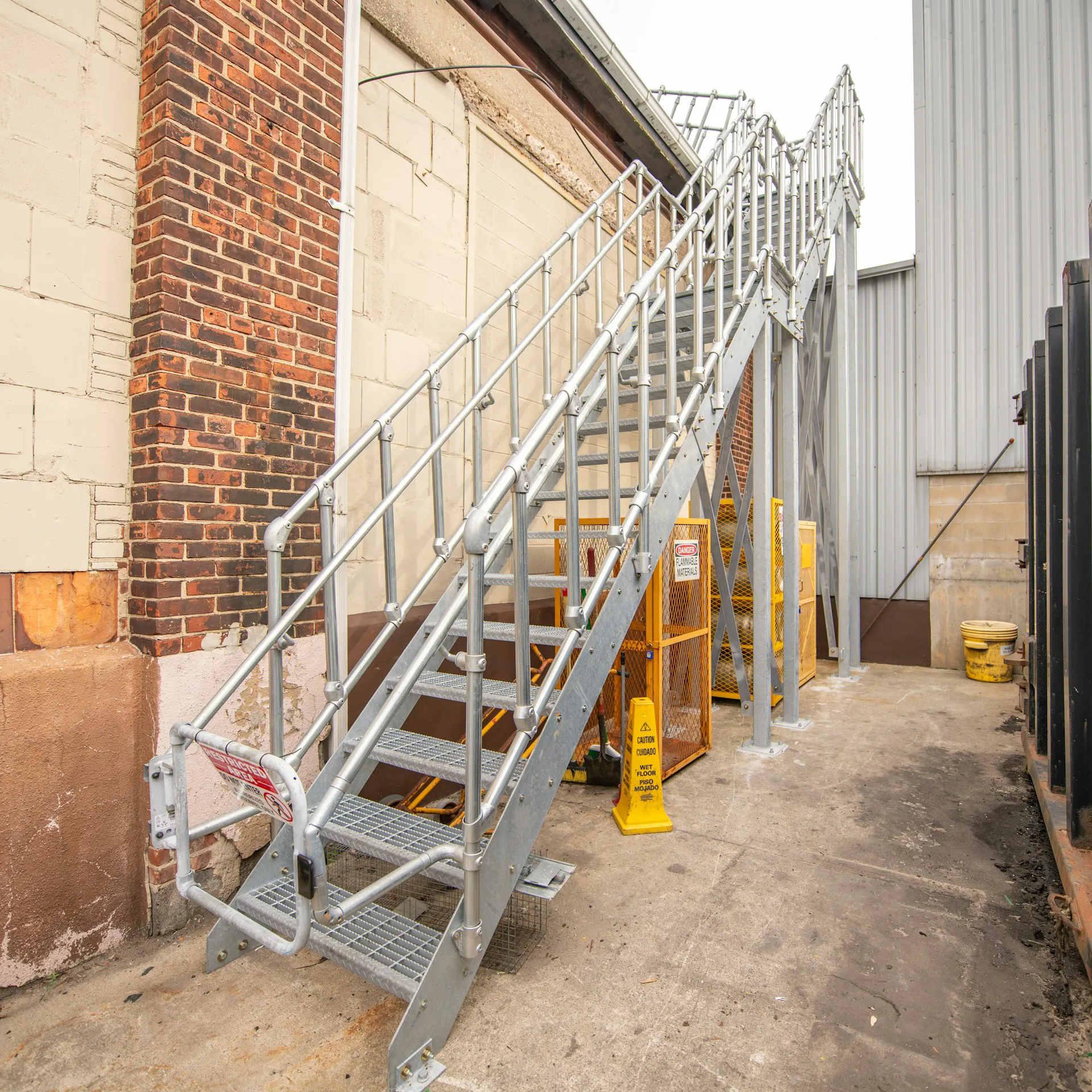Stalen trap met leuningen aan de zijkant, geplaatst naast een gebouw in een industriële omgeving